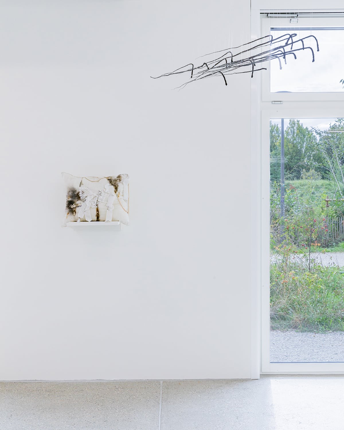 Élie Autin,<strong> </strong><em>Pillow, </em>coussin cousue main et rehaussé d’ajouts cousus, 60 x 50 cm, 2023.<em>Arrows</em>, ensemble de flèches en cheveux synthétiques trempés dans de la résine, dimensions variables, 2024, photo : Théo Dufloo.